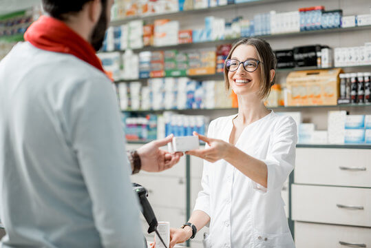 Female presenting pharmacist handing male presenting patient a prescription