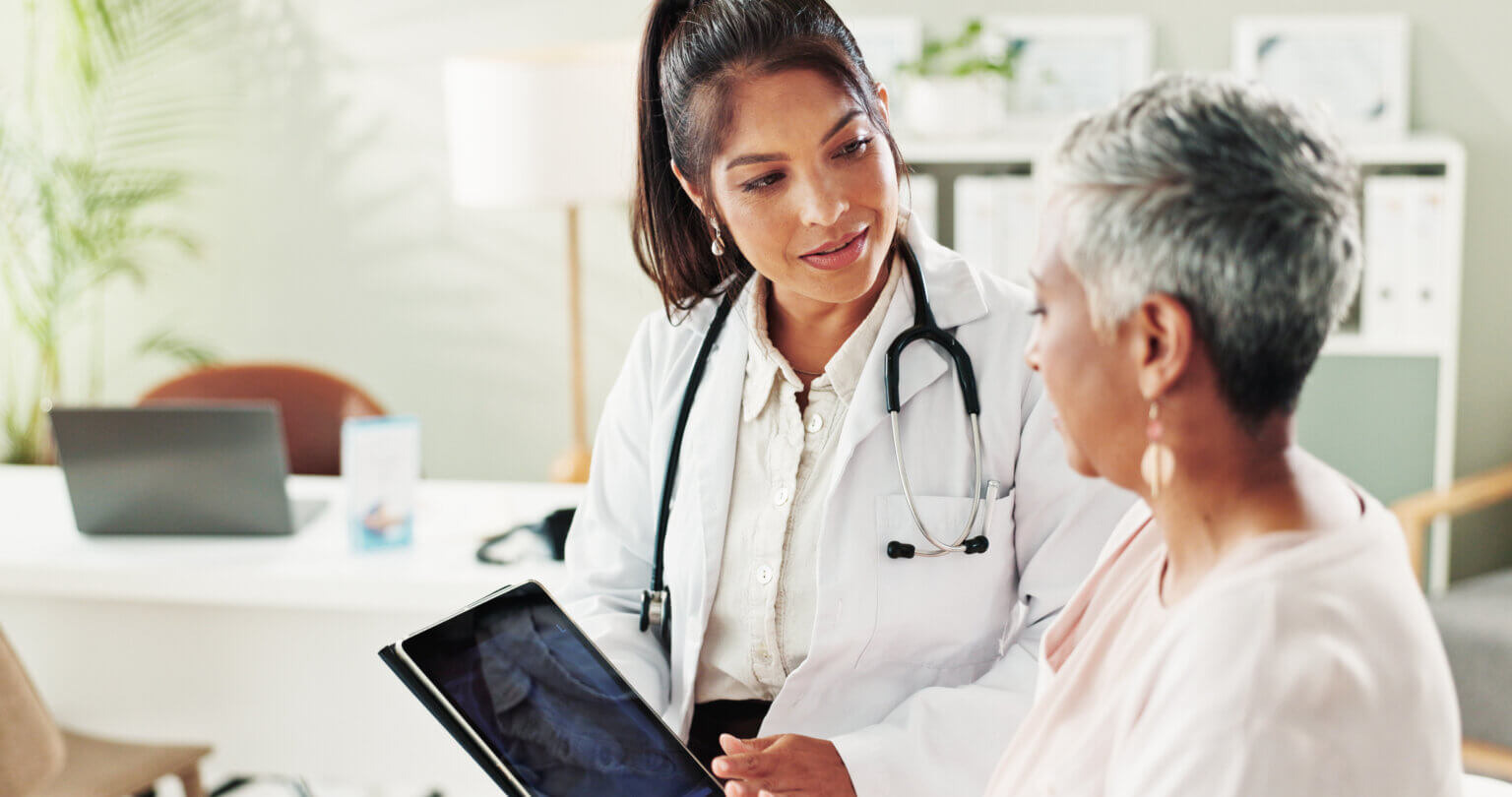 Female presenting patient looking at a tablet while consulting with a female presenting medical professional